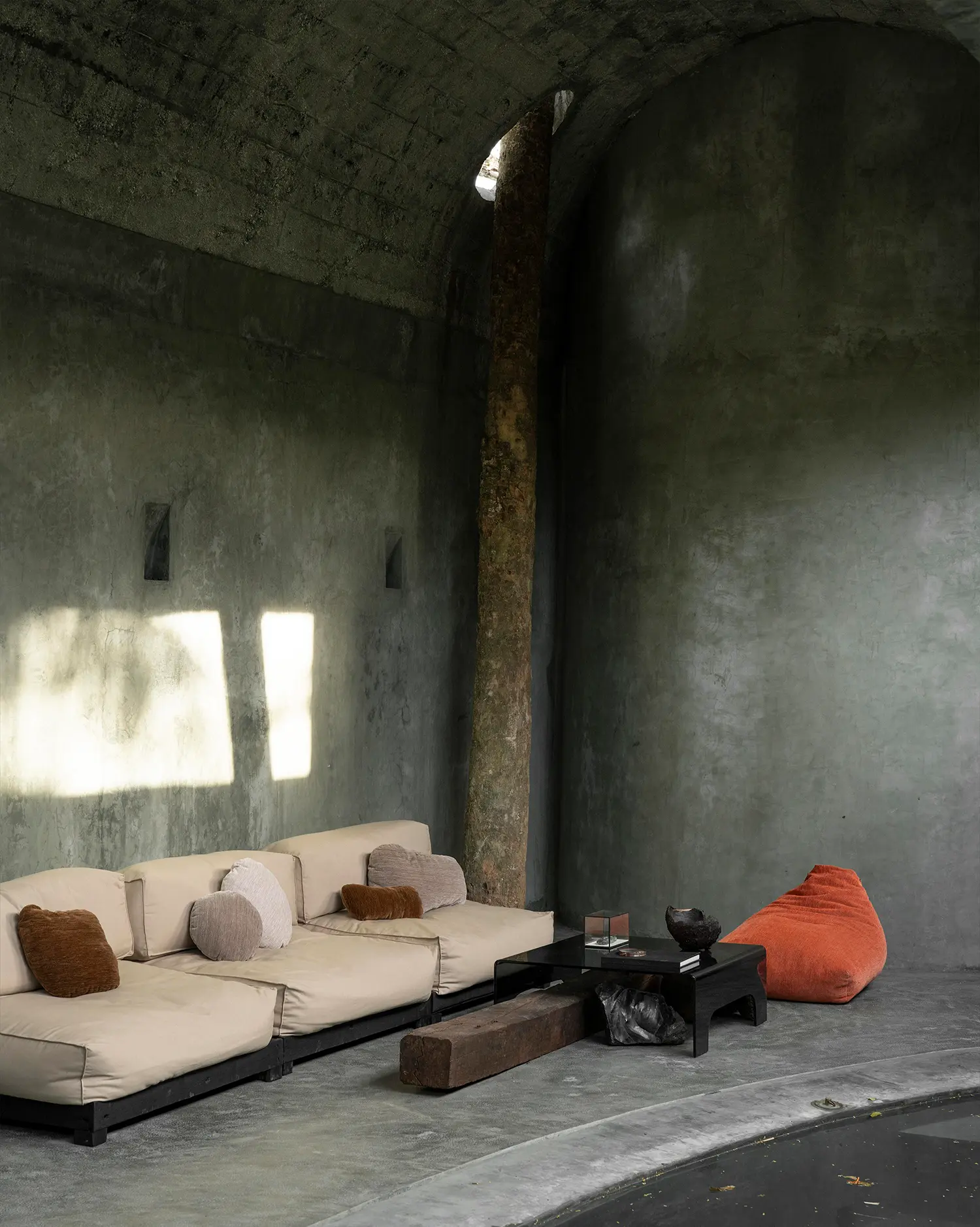 Casa Gruta vaulted concrete lounge with modular sofa and existing tree passing through a ceiling opening, Valladolid