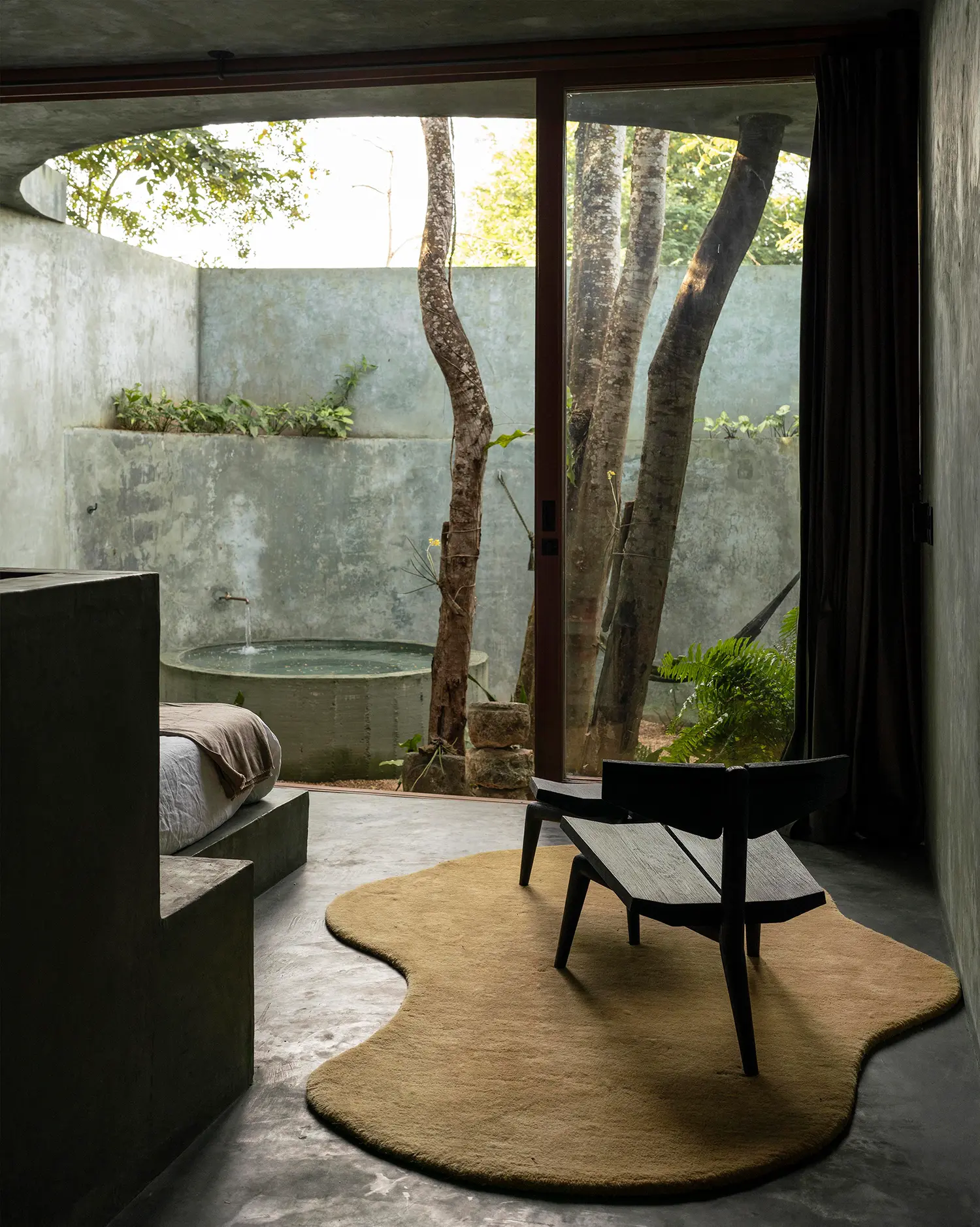 Casa Gruta bedroom in pigmented concrete with private circular water feature visible through glazing, Valladolid
