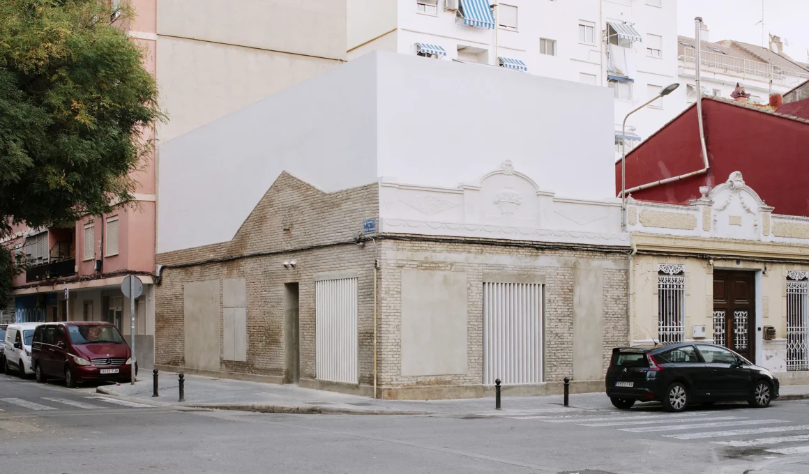 Casa Nido by Iterare Arquitectos, corner exterior in Torrefiel with preserved brick base and new white upper volume above ornate stucco cornice