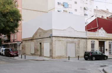 Casa Nido by Iterare Arquitectos, corner exterior in Torrefiel with preserved brick base and new white upper volume above ornate stucco cornice