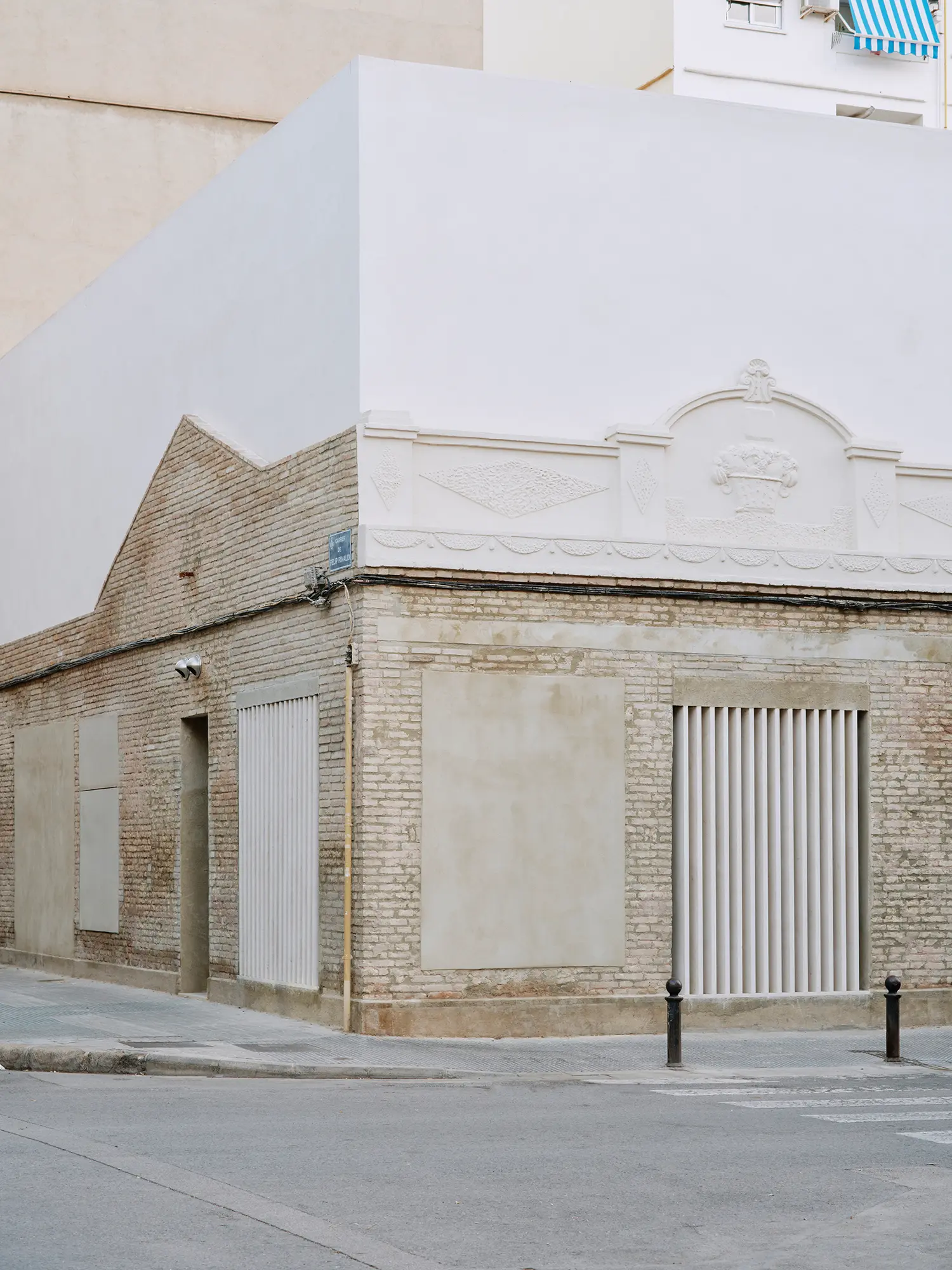 Close view of Casa Nido's preserved brick corner facade by Iterare Arquitectos, showing the original stucco relief cornice under a new white wall