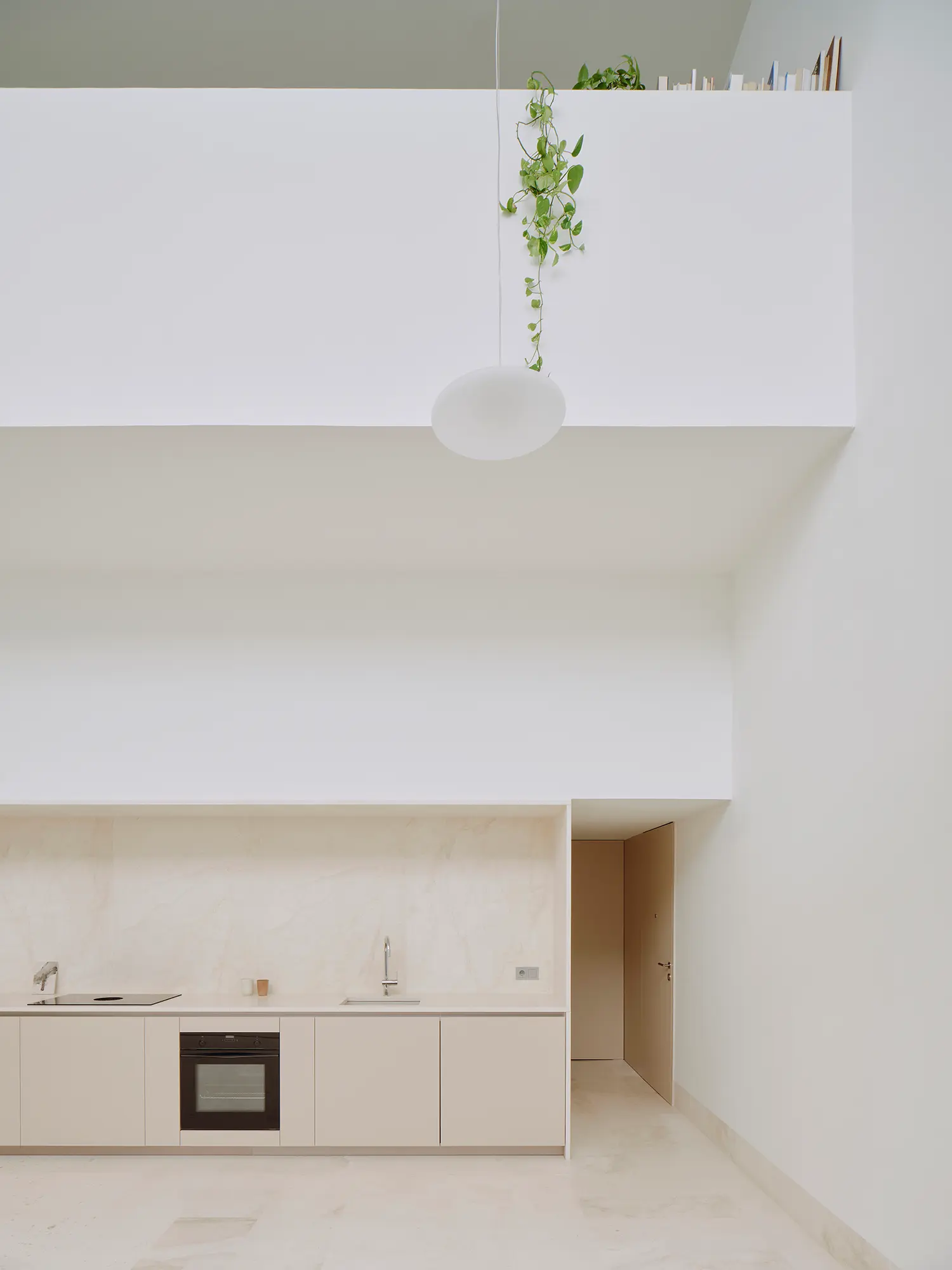 Mezzanine view over the kitchen in Casa Nido by Iterare Arquitectos, pendant light and trailing plant beneath an open bedroom door