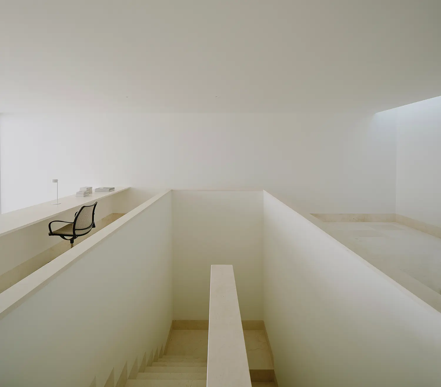 Stairwell of Casa Nido by Iterare Arquitectos, limestone-clad stair core viewed from the upper landing with a desk chair at left