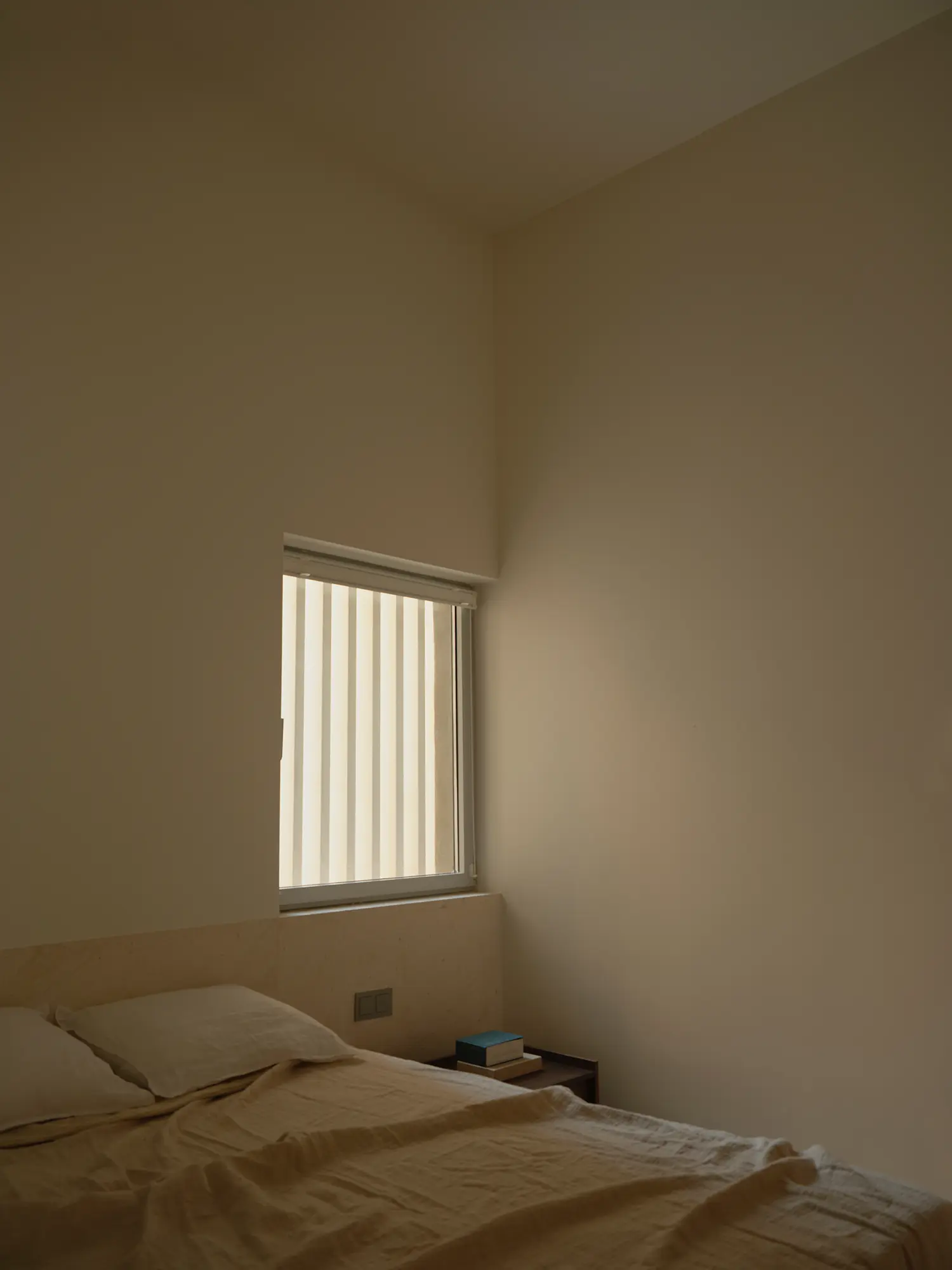 Bedroom corner in Casa Nido by Iterare Arquitectos, single vertical window with slatted blind beside an unmade bed