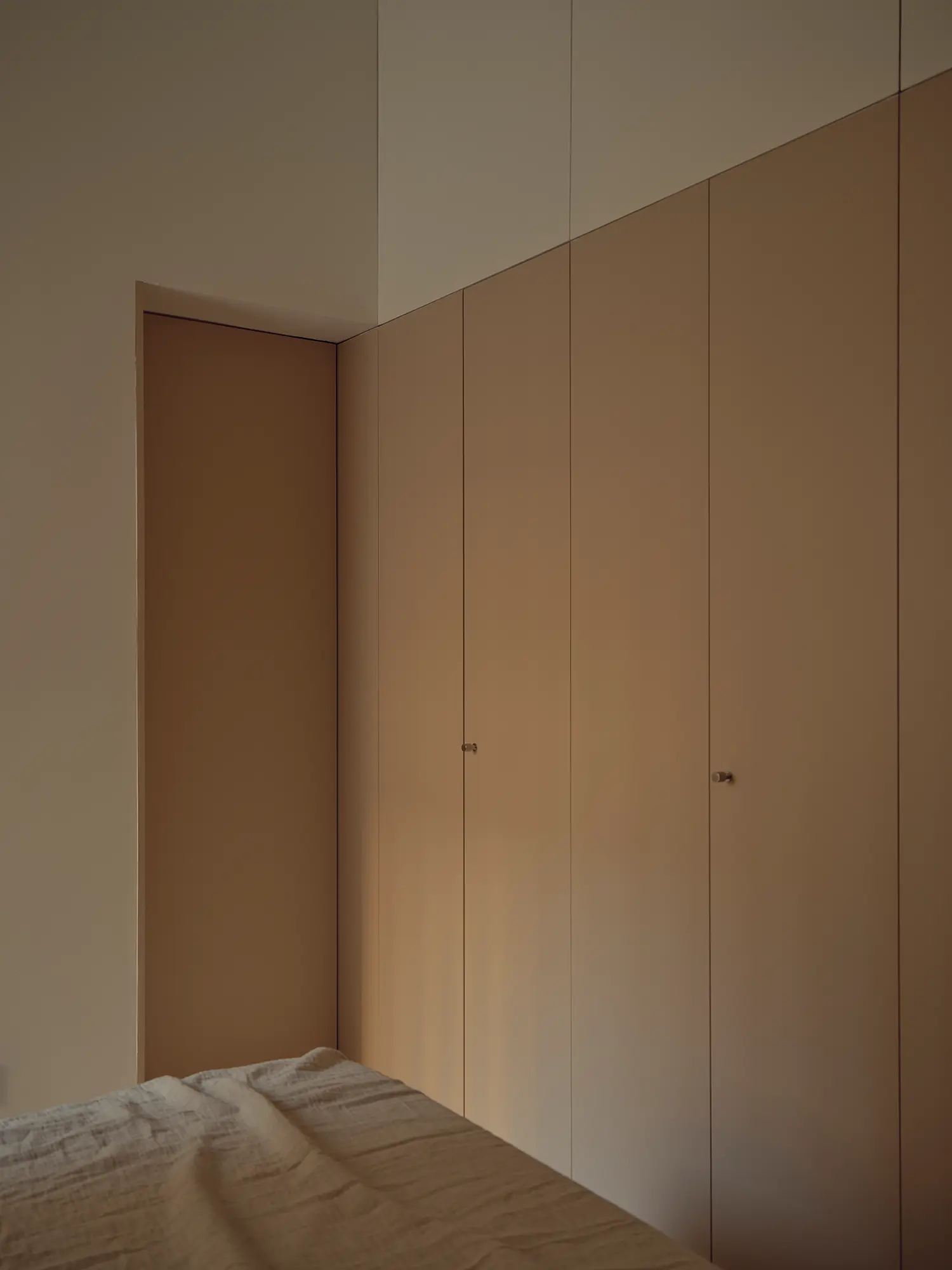 Bedroom built-in wardrobe wall in Casa Nido by Iterare Arquitectos, floor-to-ceiling timber-toned cabinetry beside a corner door