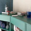 Container 03 by Atelierzero: sage-green kitchen counter against a perforated teal concrete-block wall, with moka pot and glassware