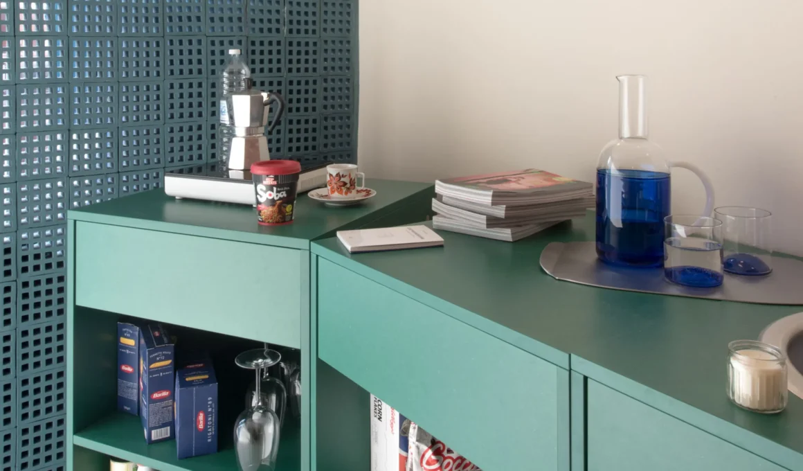 Container 03 by Atelierzero: sage-green kitchen counter against a perforated teal concrete-block wall, with moka pot and glassware