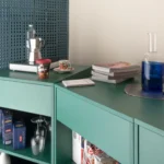 Container 03 by Atelierzero: sage-green kitchen counter against a perforated teal concrete-block wall, with moka pot and glassware