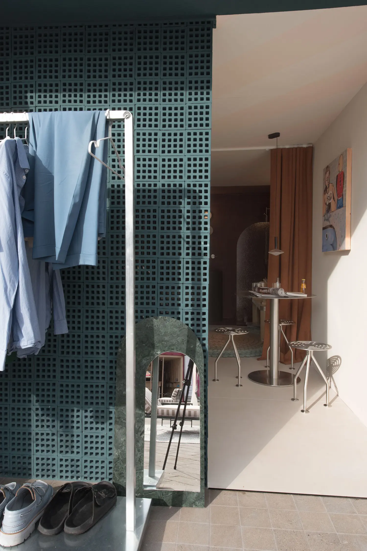 Container 03 by Atelierzero: perforated teal block wall with clothing rack and green marble arched mirror, opening onto a dining nook