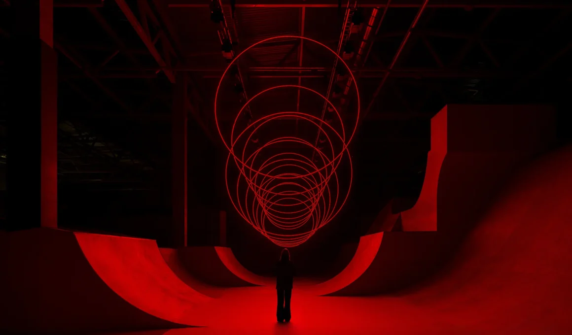 SpY's CYCLES N2 kinetic installation with red-lit rings suspended above a viewer in a ramp-lined hall in Kazan