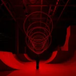 SpY's CYCLES N2 kinetic installation with red-lit rings suspended above a viewer in a ramp-lined hall in Kazan