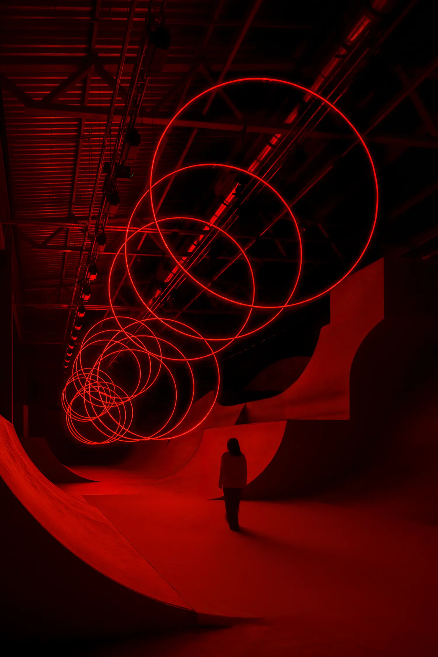 Diagonal view of SpY's CYCLES N2 rings coiling downward above a viewer inside the red-lit Kazan installation