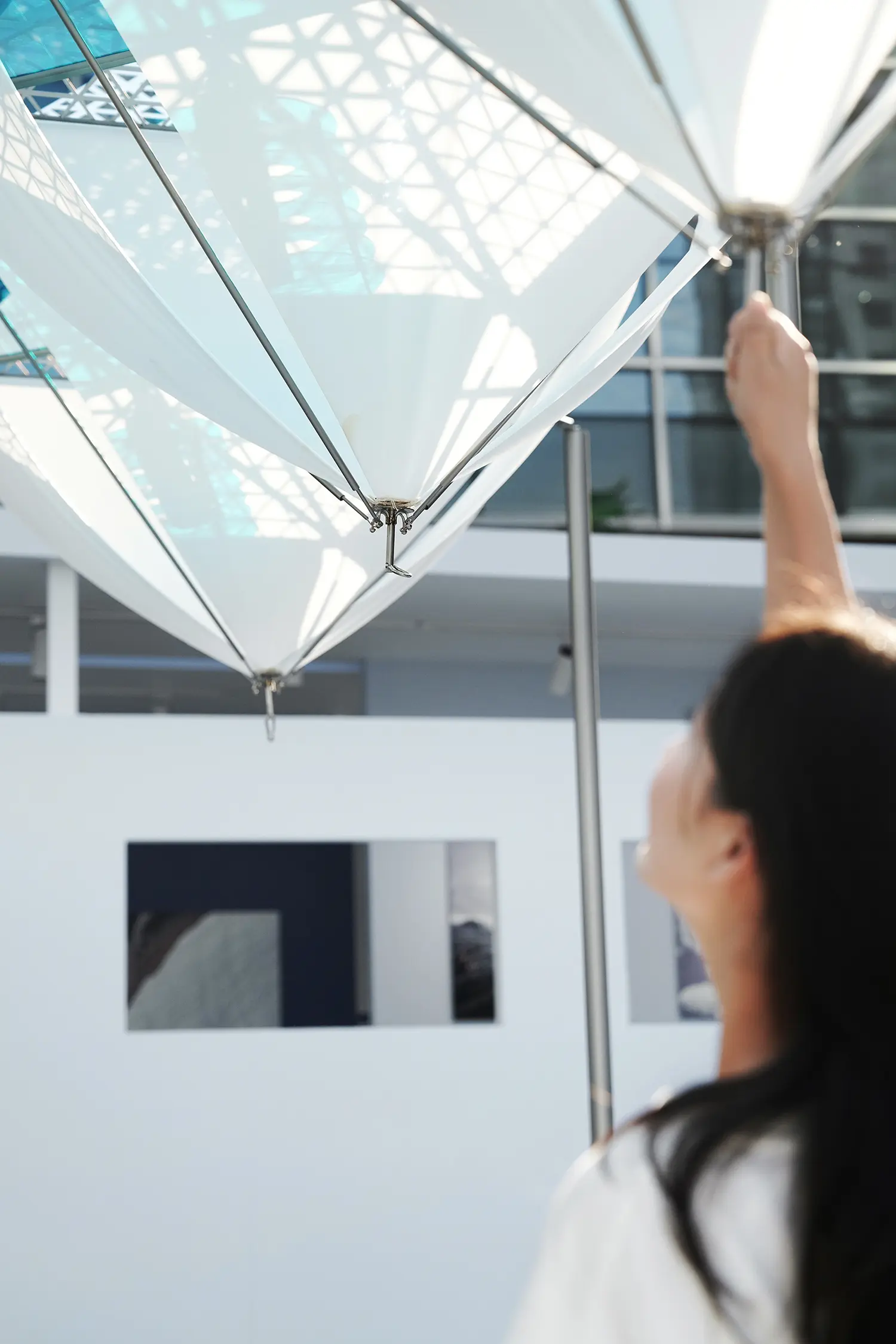 Visitor reaching up to a suspended form of Glacier Project by Dayuan Design, white fabric membranes converging on a steel node overhead