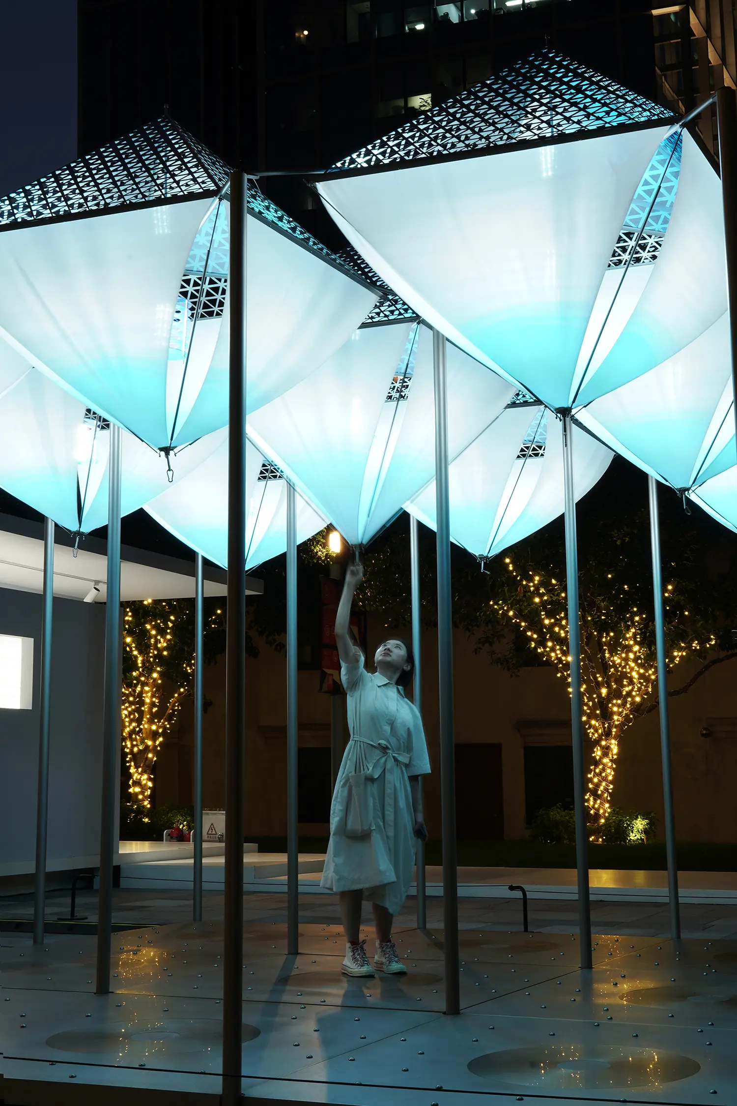 Glacier Project by Dayuan Design illuminated at night, cyan-lit suspended forms above a visitor on a reflective perforated-metal floor