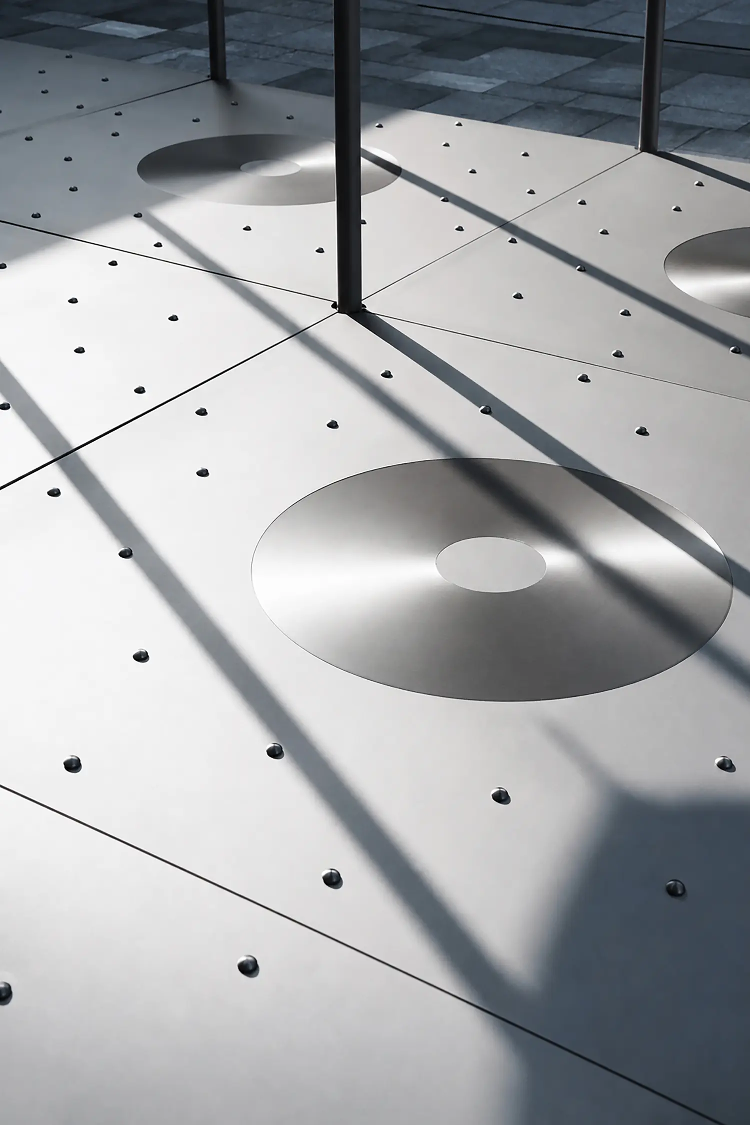 Perforated stainless-steel floor of Glacier Project by Dayuan Design with circular drainage discs and raised studs under pole shadows
