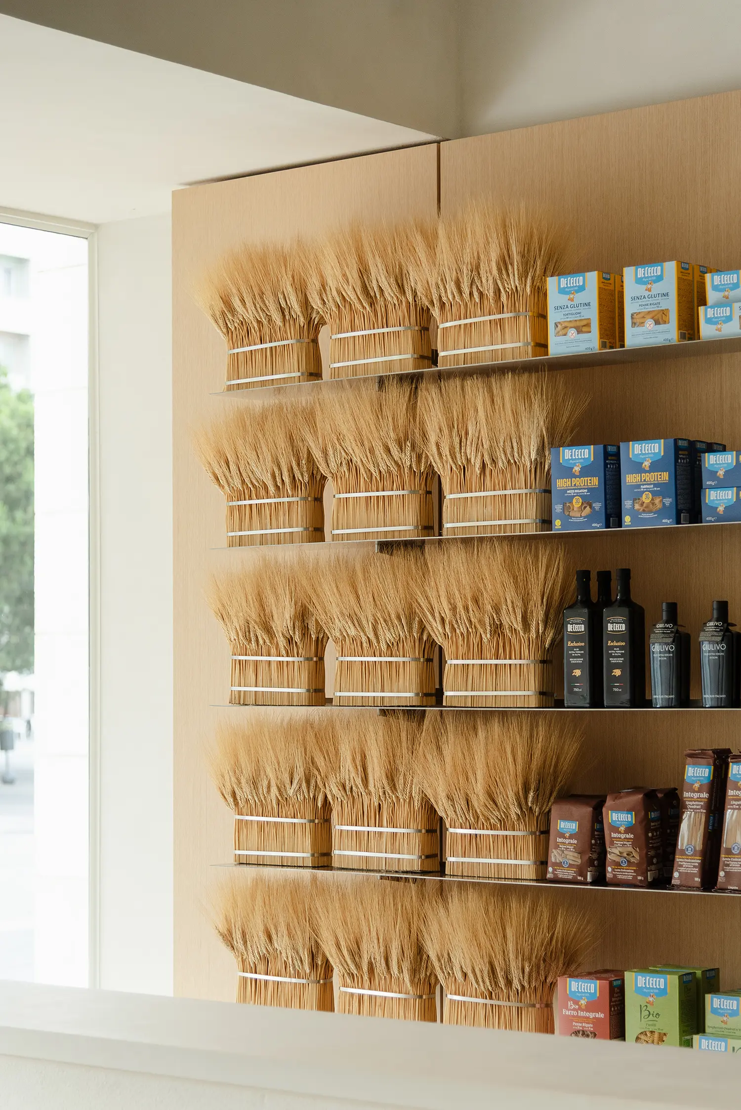 De Cecco Flagship Store by Studio Francesco Faccin, dried wheat sheaf installation on timber wall, glass shelving, oil bottles and pasta packaging