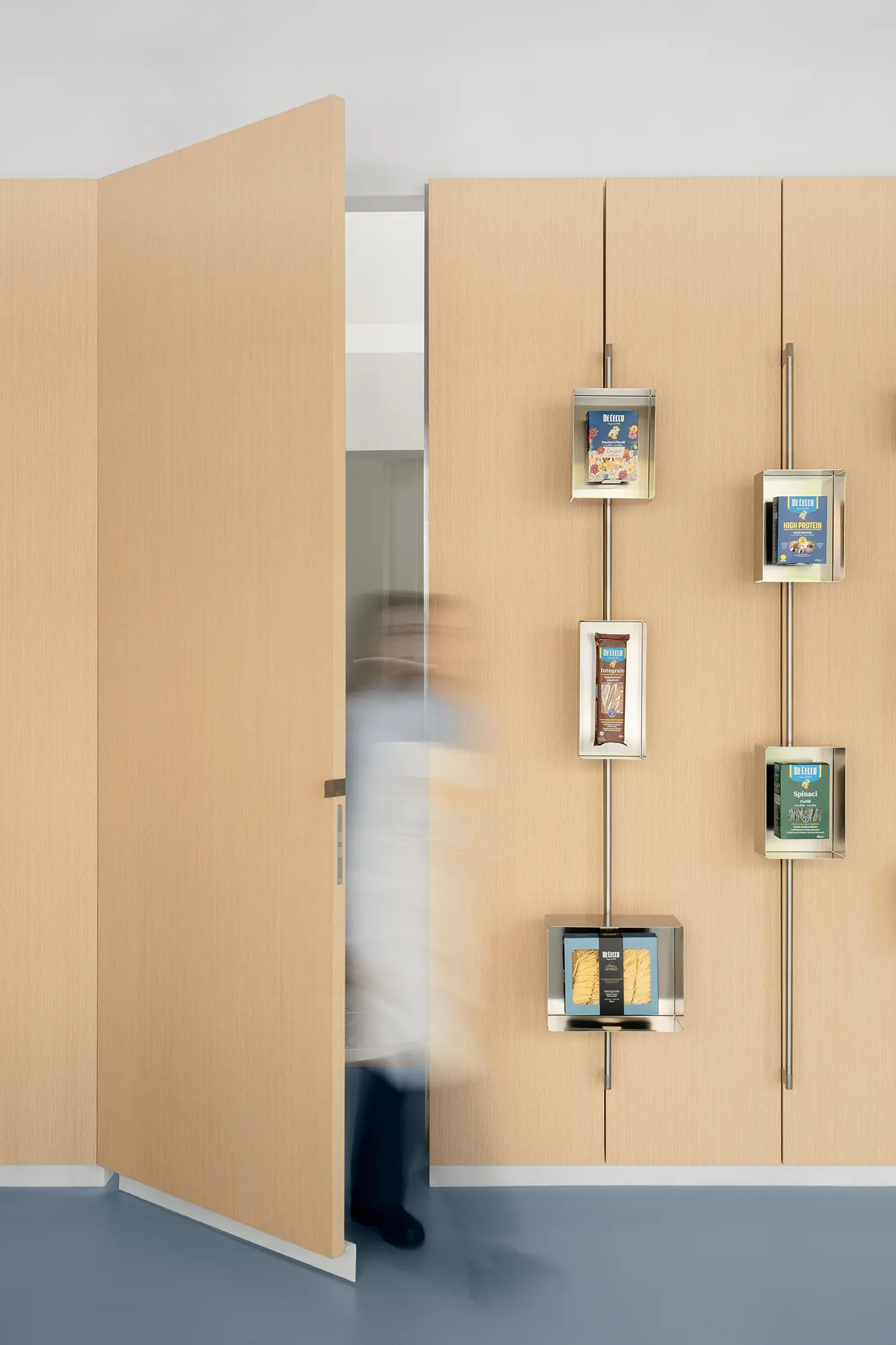 De Cecco Flagship Store by Studio Francesco Faccin, timber wall with steel display frames, wooden door ajar, blurred figure passing through