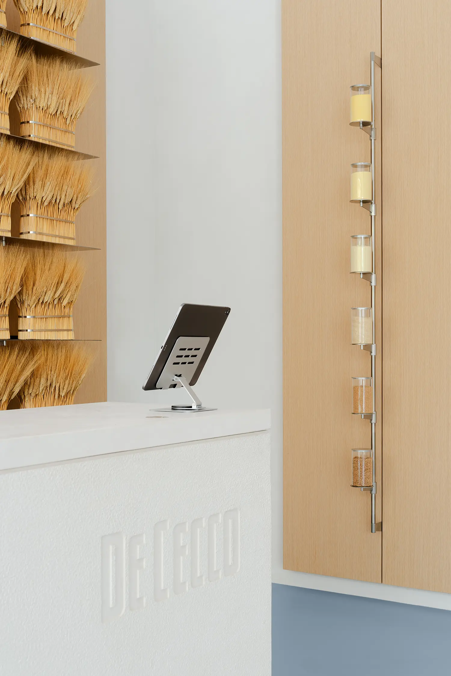De Cecco Flagship Store by Studio Francesco Faccin, vertical steel display holding glass cylinders with wheat grain samples at stages of milling, checkout counter with tablet POS, De Cecco logo engraved in stone