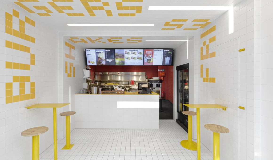 Interior of Fab Fries Freddy by Ninetynine, Amsterdam, showing white tile walls and ceiling narrowing toward a red-tiled prep counter
