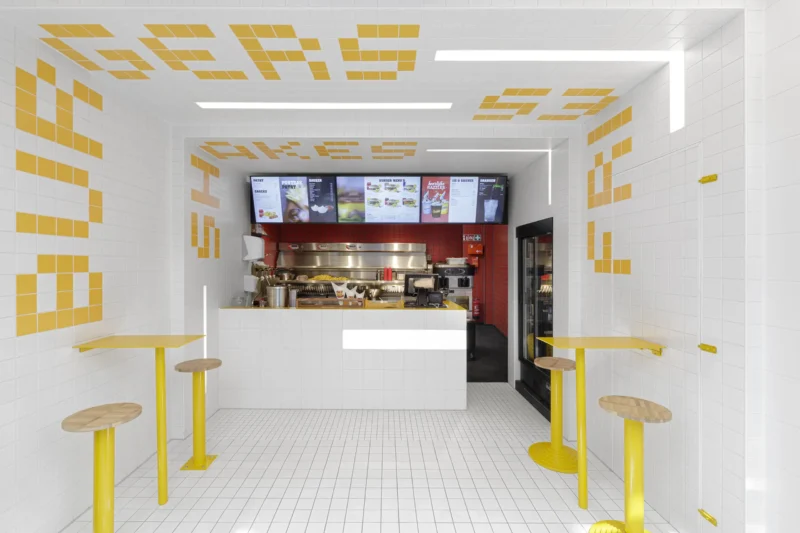 Interior of Fab Fries Freddy by Ninetynine, Amsterdam, showing white tile walls and ceiling narrowing toward a red-tiled prep counter