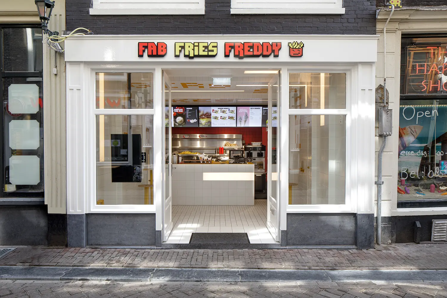 Exterior of Fab Fries Freddy by Ninetynine in Amsterdam, pixel-art signage above an open white-framed doorway on Oudebrugsteeg
