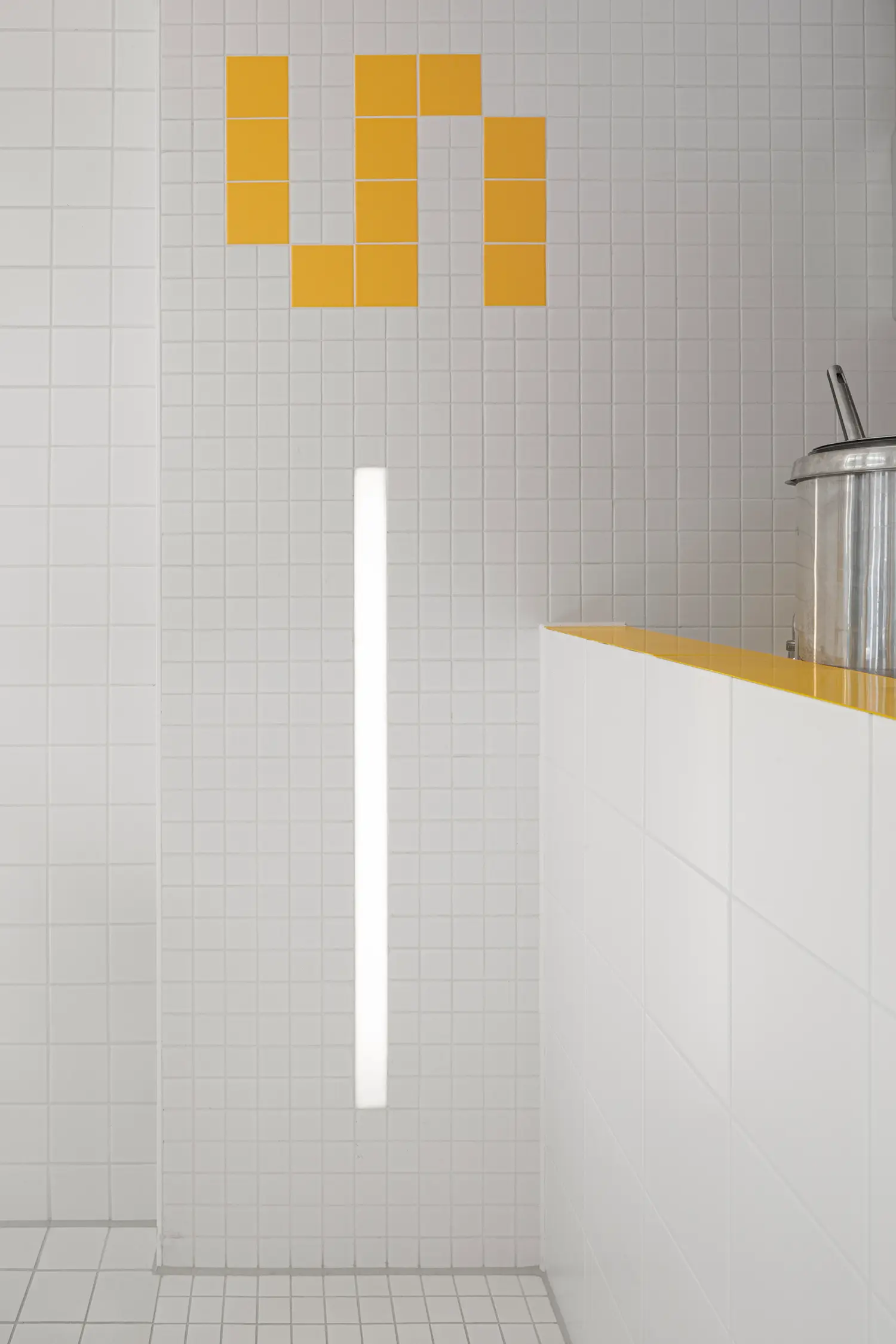 Detail of counter edge at Fab Fries Freddy by Ninetynine, Amsterdam, showing yellow powder-coated steel trim against white ceramic wall tile