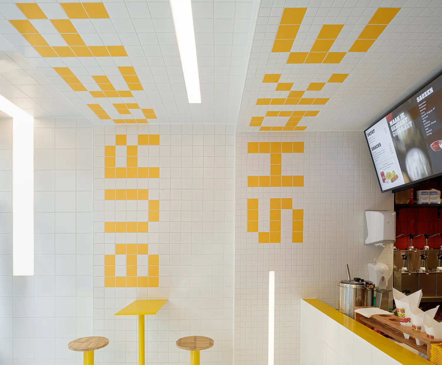Detail of Fab Fries Freddy's yellow tile lettering on ceiling and walls by Ninetynine, with red-tiled prep area and menu screen visible