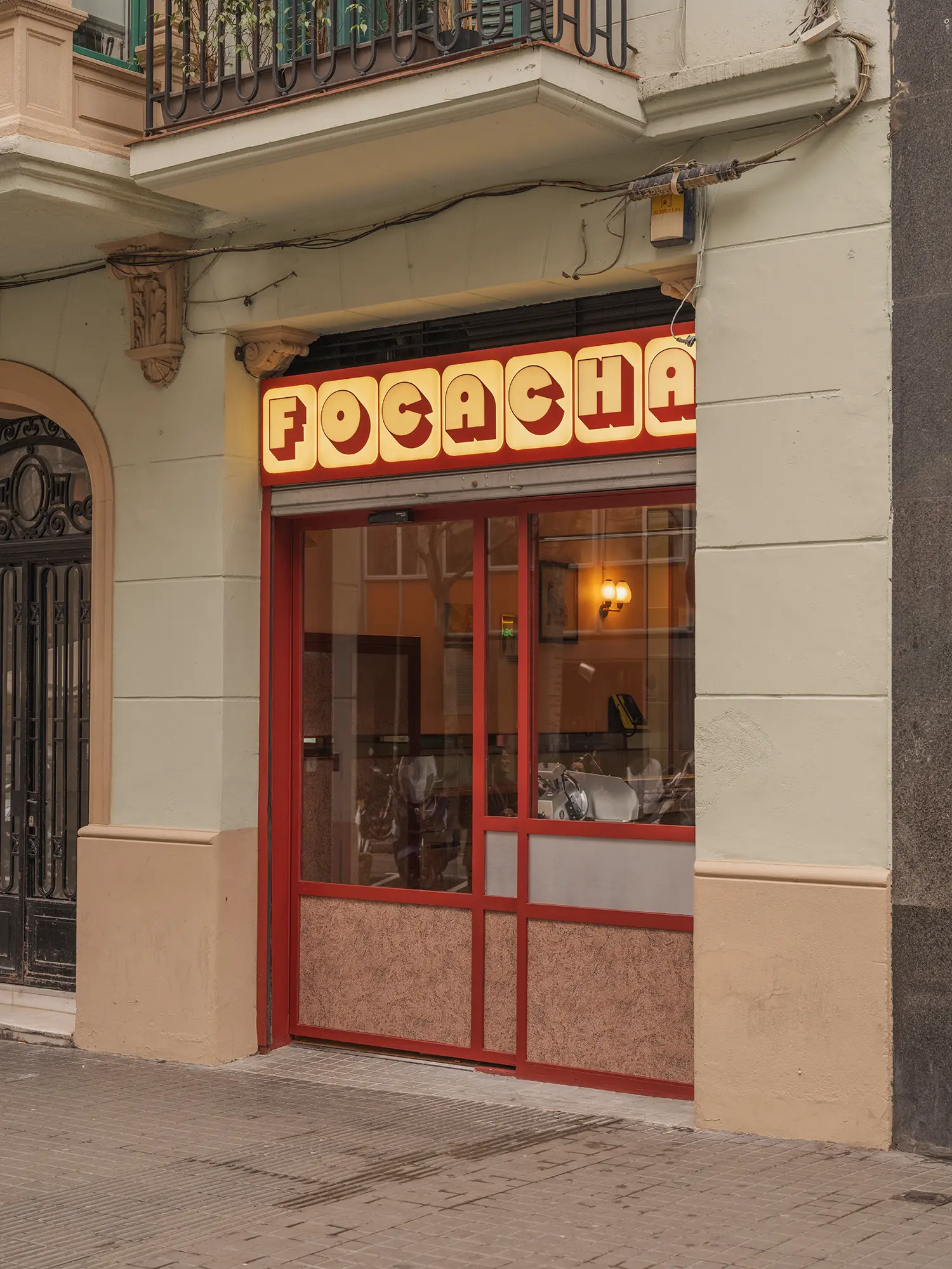 Focacha storefront by Isern Serra on Carrer Tuset, Barcelona, illuminated retro signage above a modest glazed focacceria entrance
