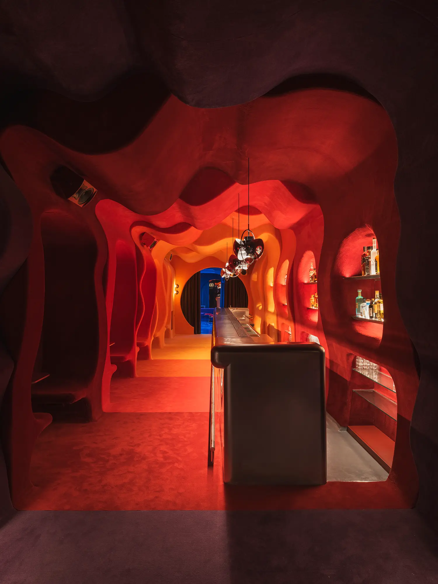 Bar room of Focacha by Isern Serra, red organic tunnel with stainless-steel counter, bottle niches and a circular doorway to a blue room
