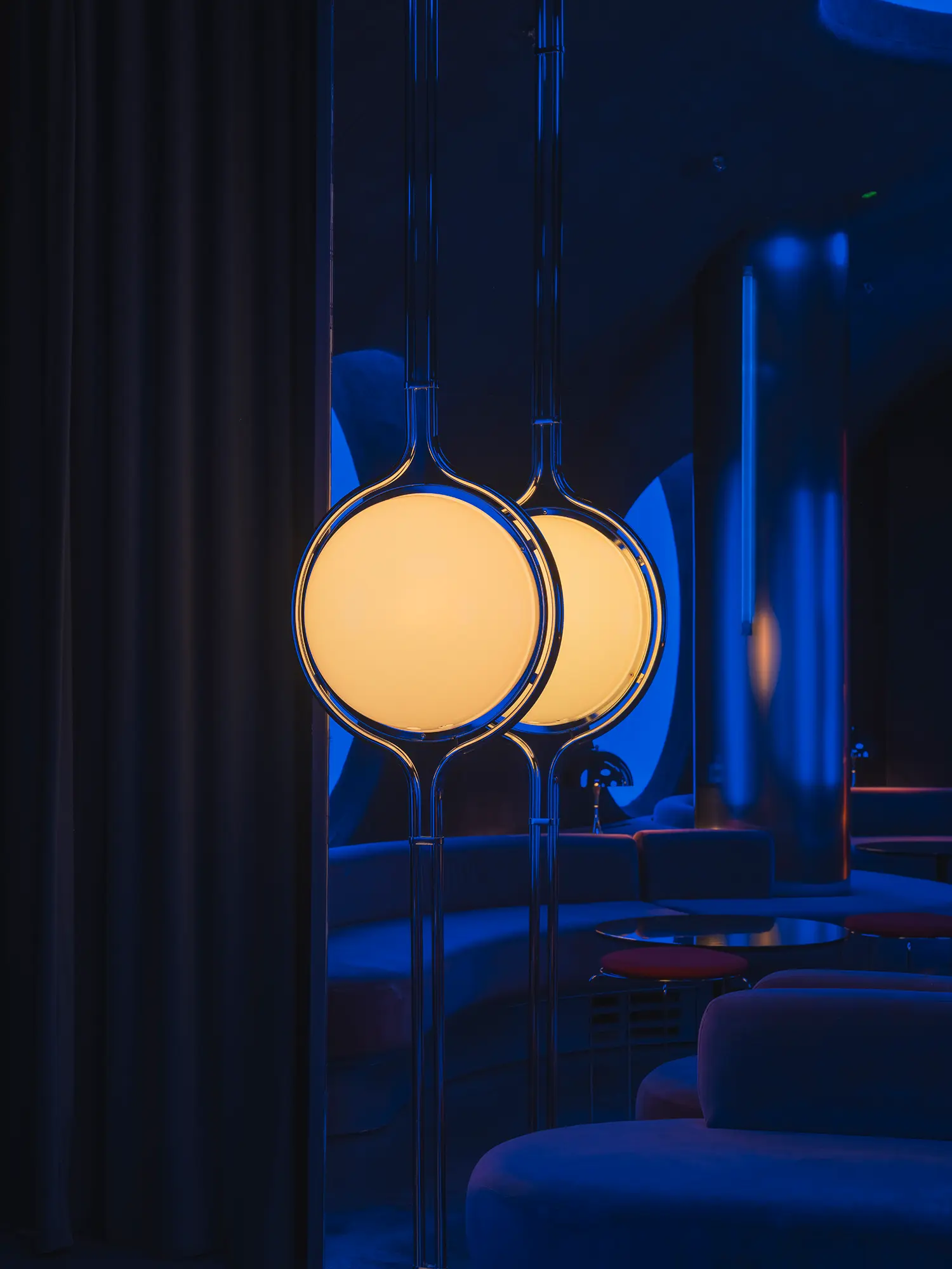 Detail of two illuminated globe pendant lamps inside Focacha by Isern Serra, glowing warm against the blue-lit interior