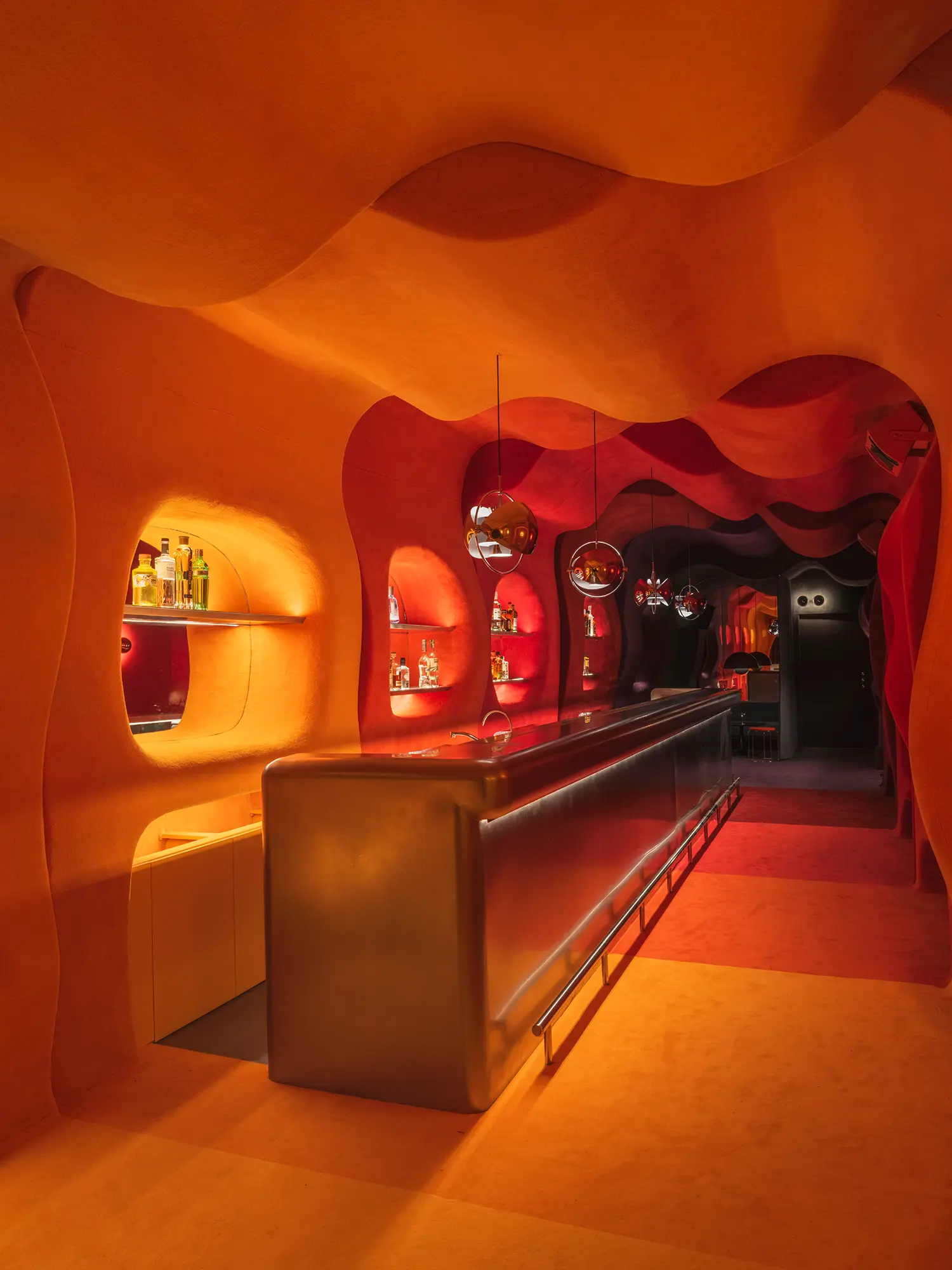 Bar counter in Focacha by Isern Serra, orange-lit organic tunnel with mirrored pendant lighting and backlit bottle display niches