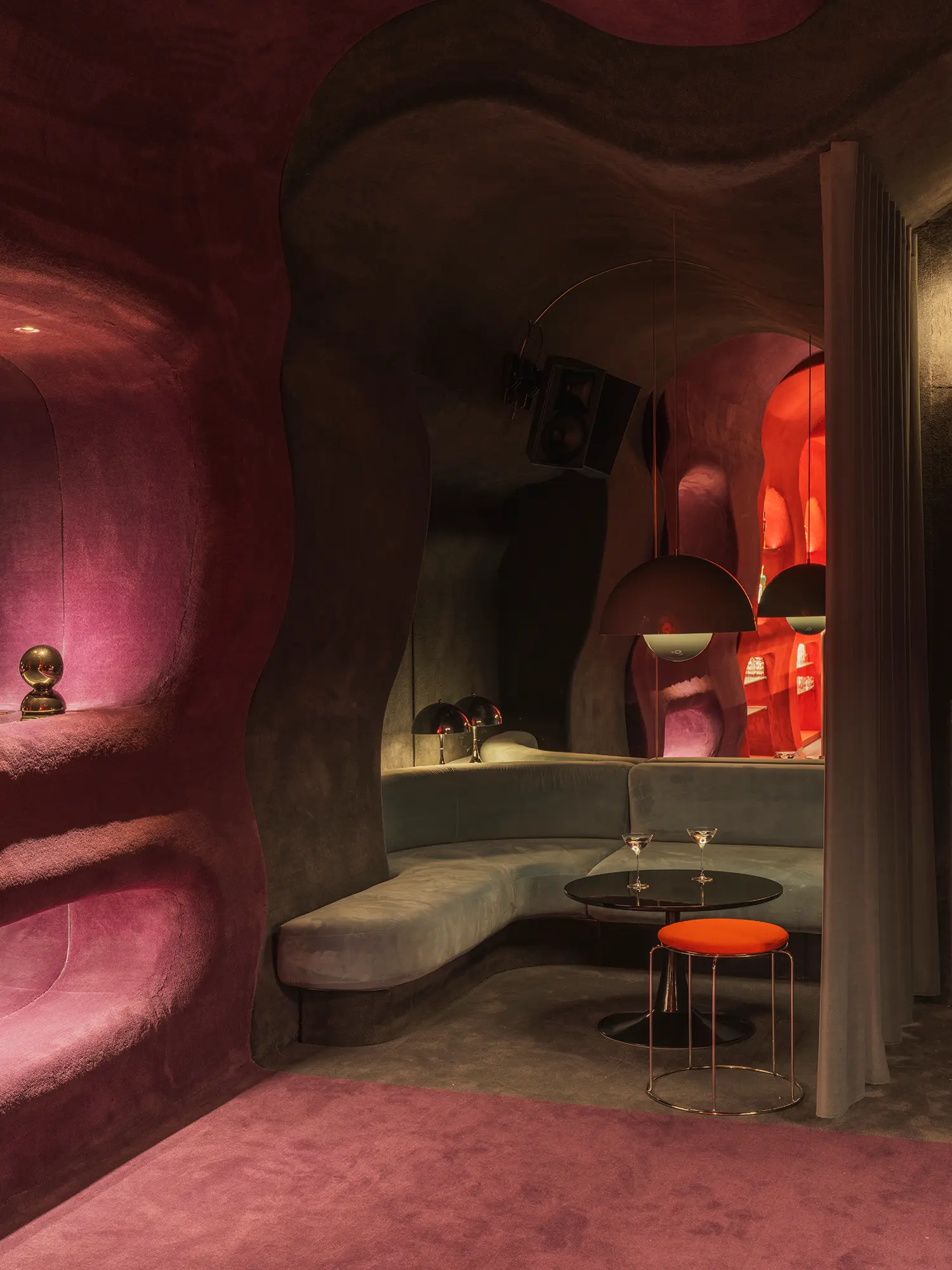 Pink-lit lounge niche in Focacha by Isern Serra, curved banquette, round cocktail table with martini glasses and dome pendant lamps