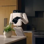 Genesis AI's Eno robot watering a potted fern on a kitchen island, gripping a watering can with its dexterous hand