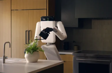 Genesis AI's Eno robot watering a potted fern on a kitchen island, gripping a watering can with its dexterous hand