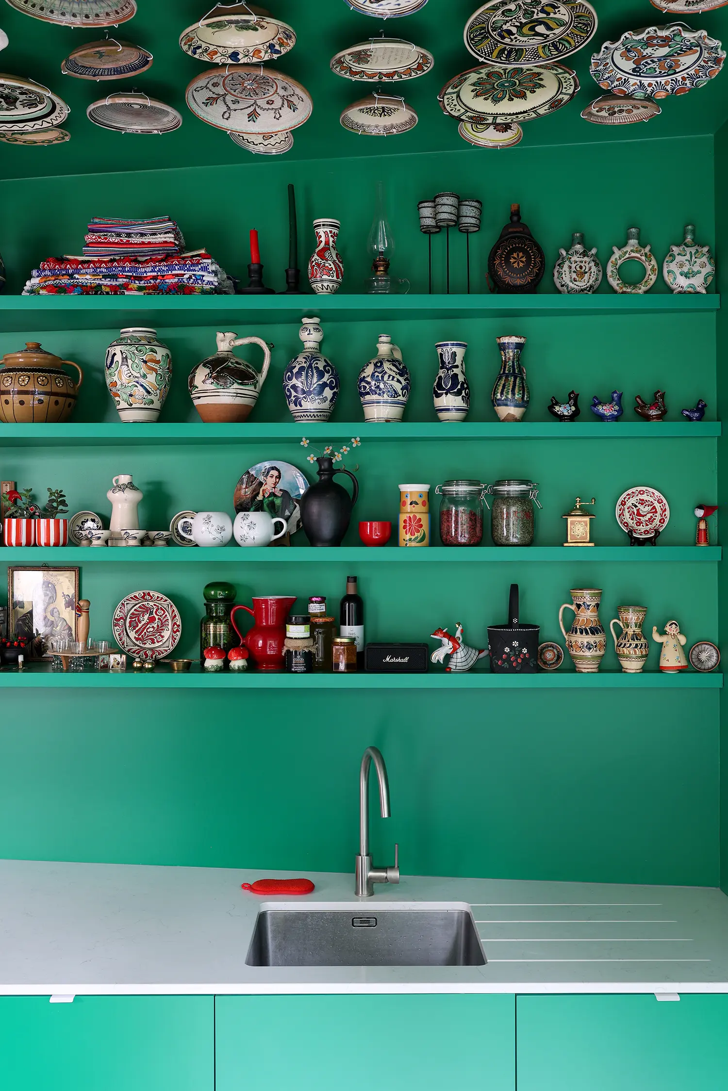 Tine Loncin Brussels kitchen shelving detail — Romanian ceramic jugs, vases, folk objects against emerald green