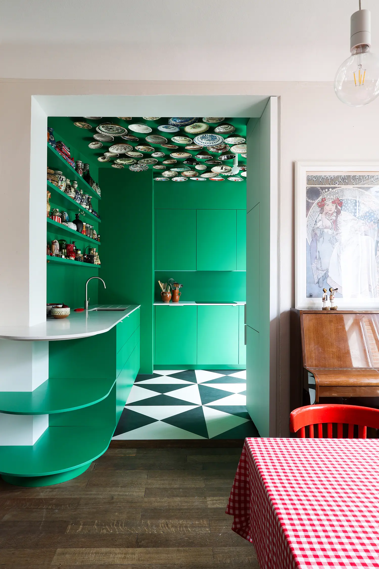Tine Loncin Brussels kitchen — emerald green cabinetry and ceiling, folk plate collection, checkerboard floor
