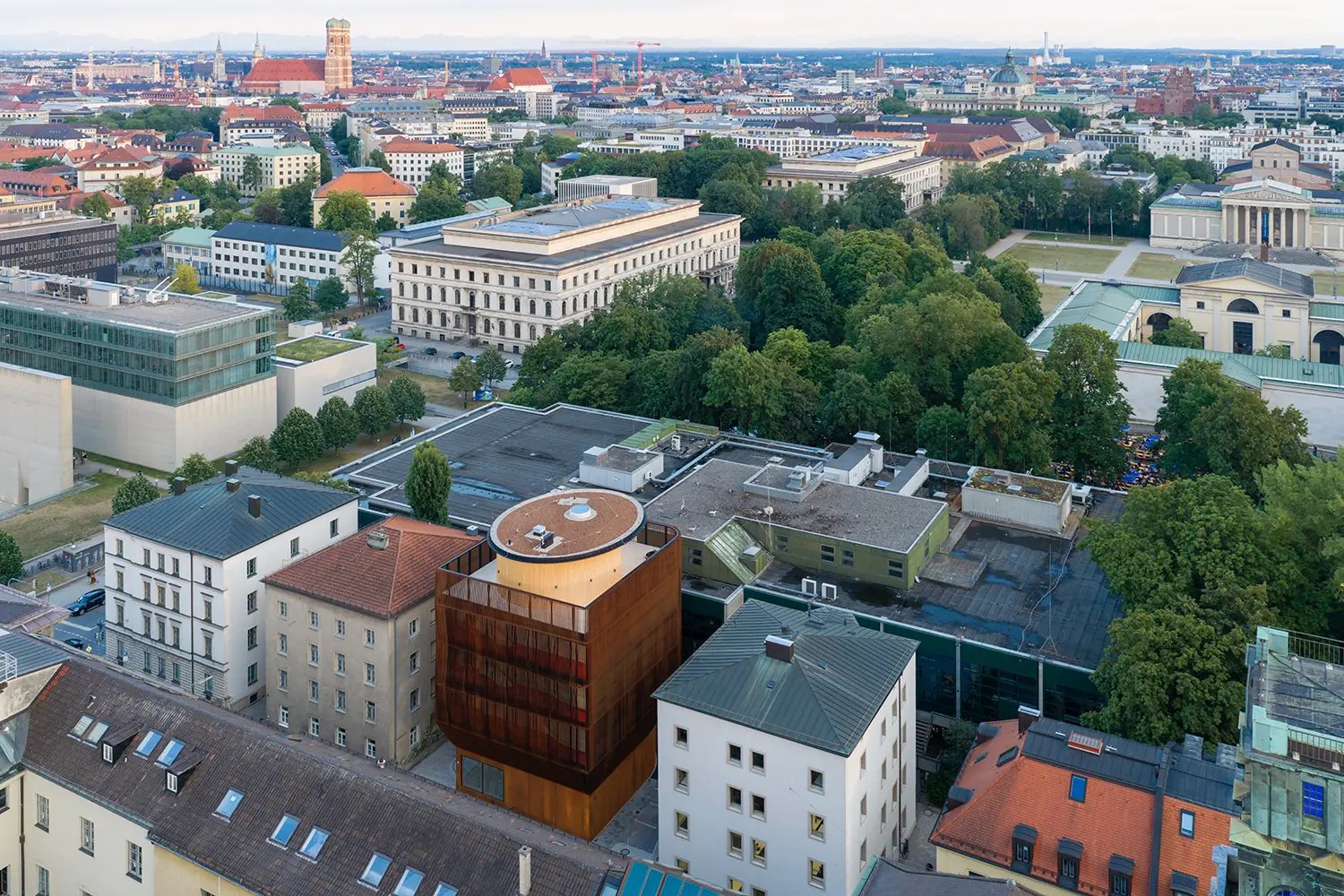 Aerial view of Kéré Architecture's timber kindergarten among Munich rooftops, with the city center and Frauenkirche towers beyond