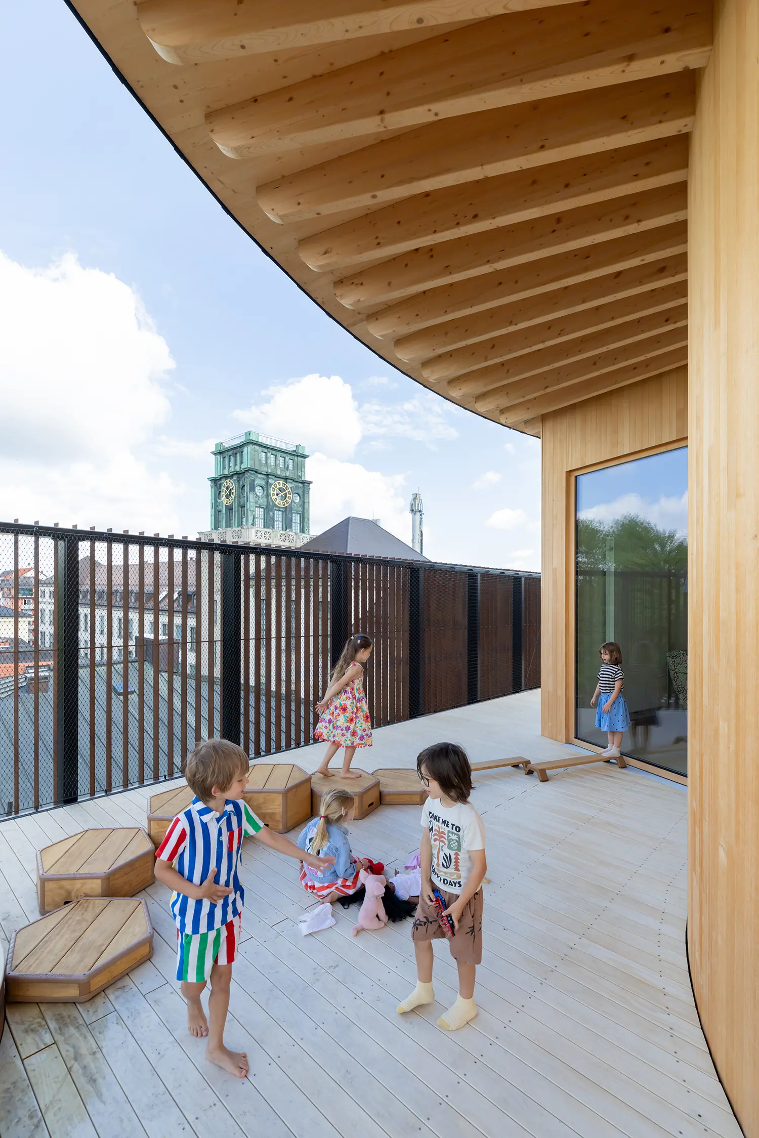 Rooftop terrace of the Kinderoase an der TUM by Kéré Architecture, children playing on timber decking with the Munich skyline beyond