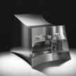 La Marzocco Linea Mini by CALIPER for Heliot Emil x Joe & The Juice, front three-quarter view, curved polished stainless steel housing, black studio background