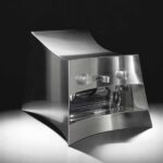 La Marzocco Linea Mini by CALIPER for Heliot Emil x Joe & The Juice, front three-quarter view, curved polished stainless steel housing, black studio background