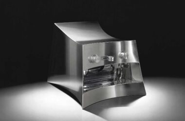 La Marzocco Linea Mini by CALIPER for Heliot Emil x Joe & The Juice, front three-quarter view, curved polished stainless steel housing, black studio background