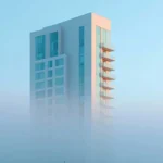 Modern white residential tower with balconies partially obscured by fog, blue sky background, real estate development exterior