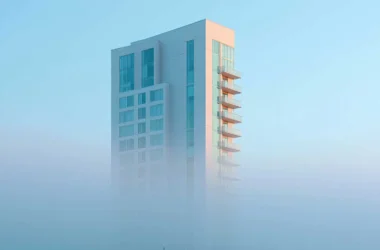 Modern white residential tower with balconies partially obscured by fog, blue sky background, real estate development exterior