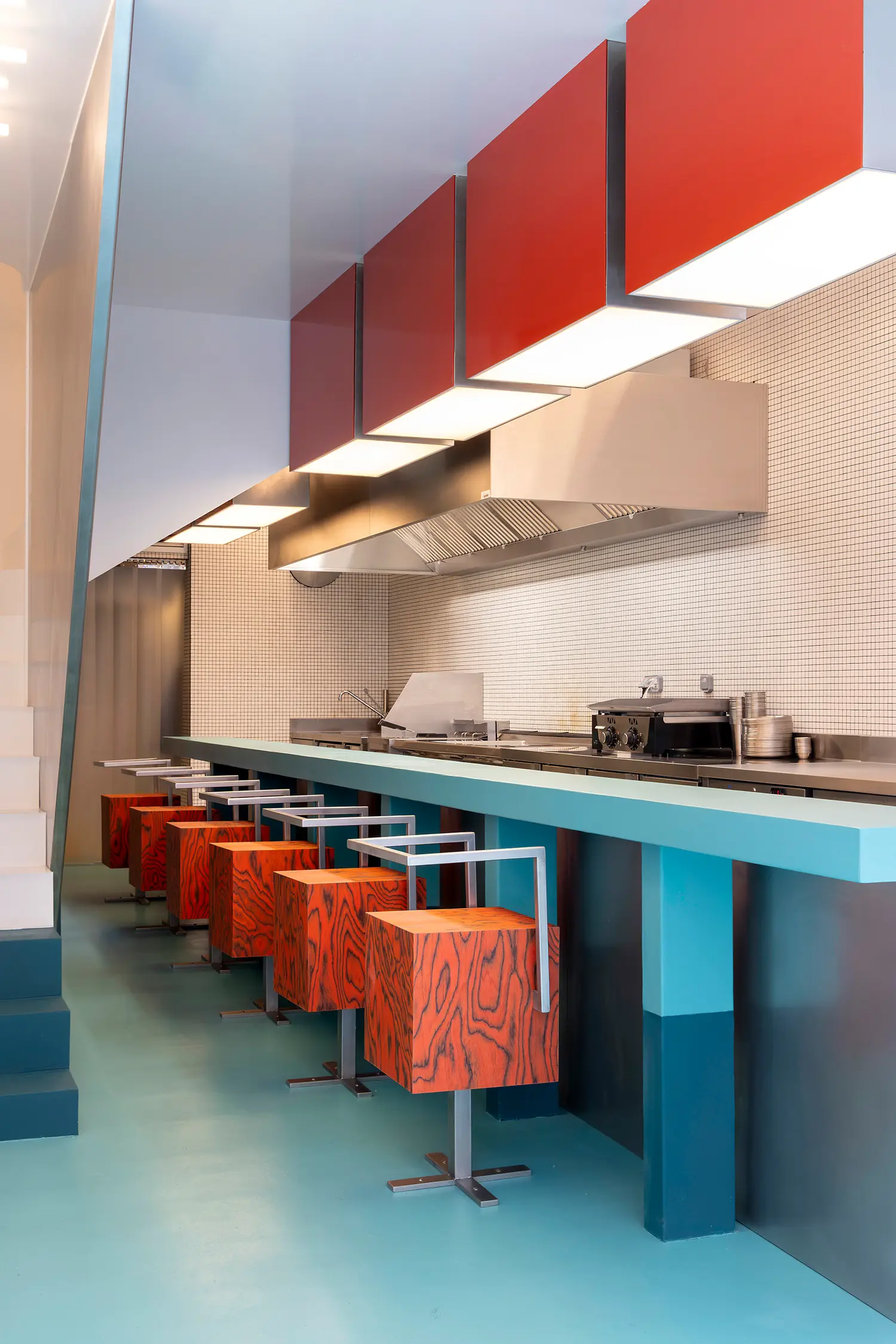 Sainto by Mur Mur, red wood veneer cube stools lined beneath red overhead panels and kitchen counter