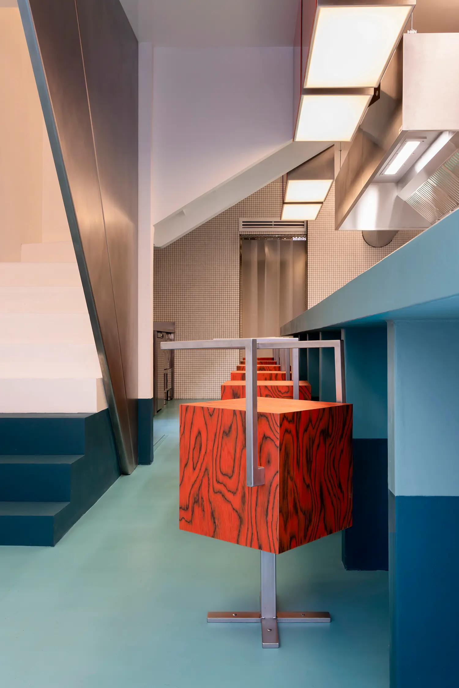 Sainto by Mur Mur, close-up of red wood veneer cube stool with stainless steel handle near staircase