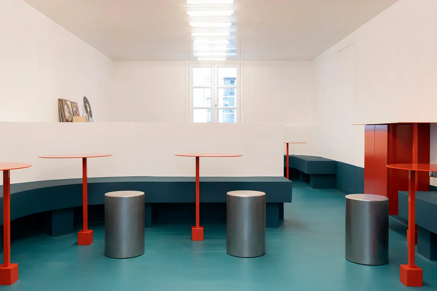 Sainto by Mur Mur, upstairs dining room with curved banquette, red round tables, and cylindrical steel stools
