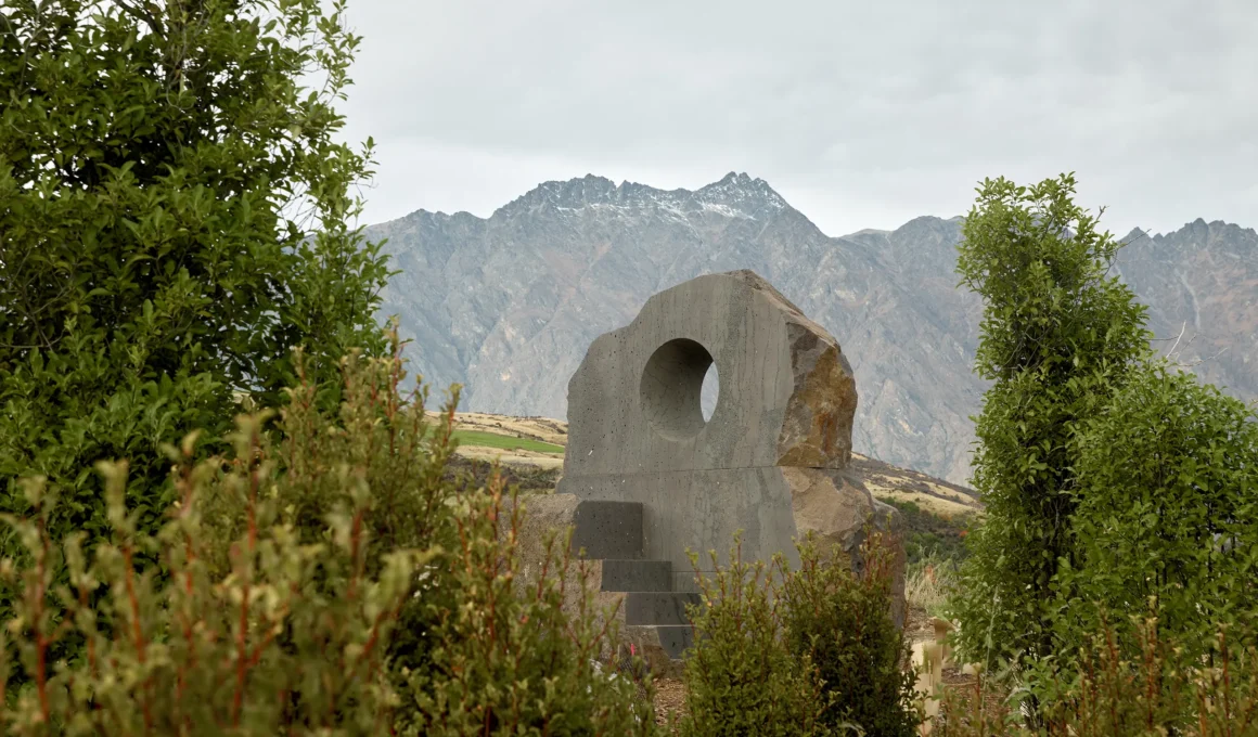 Interlude stone seat by Nebbia framed through foliage in Jardine Park with Queenstown mountains behind
