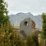Interlude stone seat by Nebbia framed through foliage in Jardine Park with Queenstown mountains behind