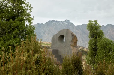 Interlude stone seat by Nebbia framed through foliage in Jardine Park with Queenstown mountains behind