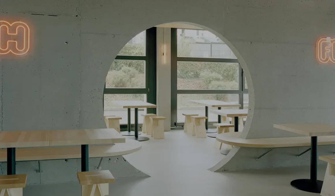 Eleventhfloor Restaurant by Noue Studio, Granges-Paccot — circular concrete cutout wall with wood benches and stools, neon signage